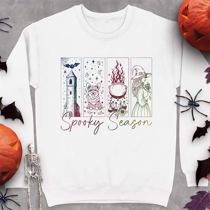 A white sweatshirt with a four-panel Halloween graphic of a haunted tower, a bandage-wrapped Corgi mummy, a bubbling cauldron with potion bottles and a witch holding flowers, with the text Spooky Season