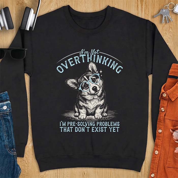 Black sweatshirt with a vintage-style illustration of a corgi wearing round glasses, and the text I'm Not Overthinking, I'm Pre-Solving Problems That Do Not Exist Yet.