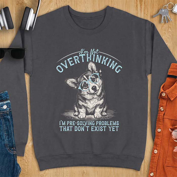 Dark Heather sweatshirt with a vintage-style illustration of a corgi wearing round glasses, and the text I'm Not Overthinking, I'm Pre-Solving Problems That Do Not Exist Yet.