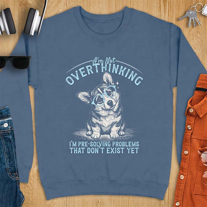 Indigo Blue sweatshirt with a vintage-style illustration of a corgi wearing round glasses, and the text I'm Not Overthinking, I'm Pre-Solving Problems That Do Not Exist Yet.