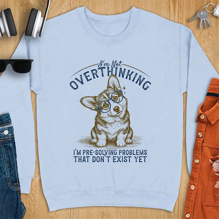 Light Blue sweatshirt with a vintage-style illustration of a corgi wearing round glasses, and the text I'm Not Overthinking, I'm Pre-Solving Problems That Do Not Exist Yet.