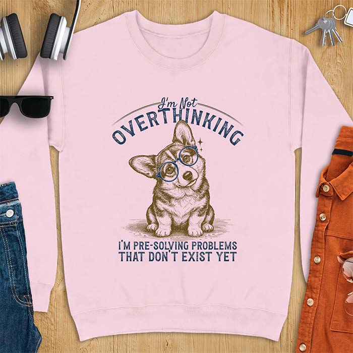 Light Pink sweatshirt with a vintage-style illustration of a corgi wearing round glasses, and the text I'm Not Overthinking, I'm Pre-Solving Problems That Do Not Exist Yet.