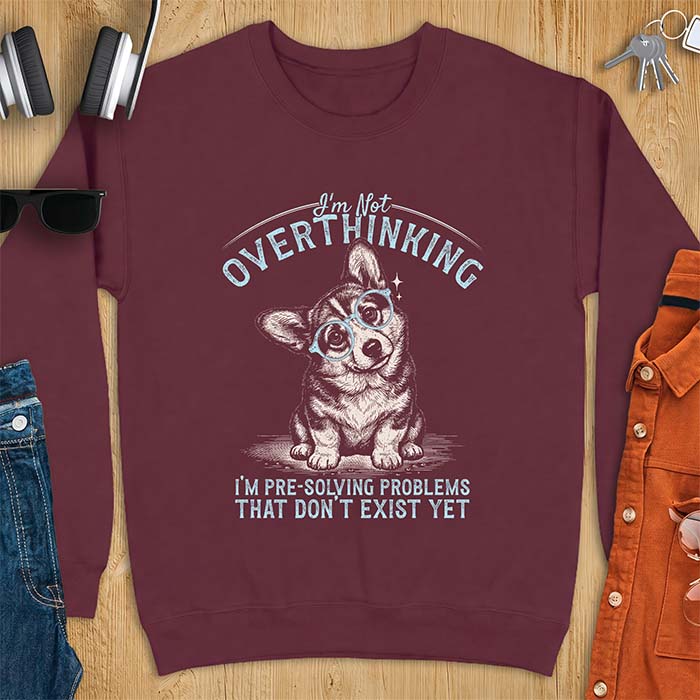 Maroon sweatshirt with a vintage-style illustration of a corgi wearing round glasses, and the text I'm Not Overthinking, I'm Pre-Solving Problems That Do Not Exist Yet.