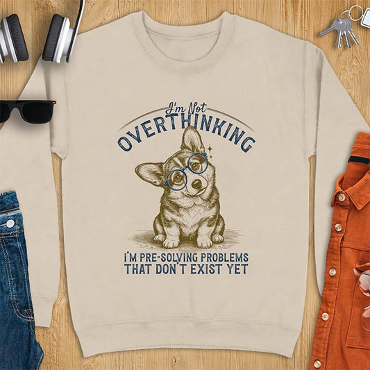 Sand sweatshirt with a vintage-style illustration of a corgi wearing round glasses, and the text I'm Not Overthinking, I'm Pre-Solving Problems That Do Not Exist Yet.