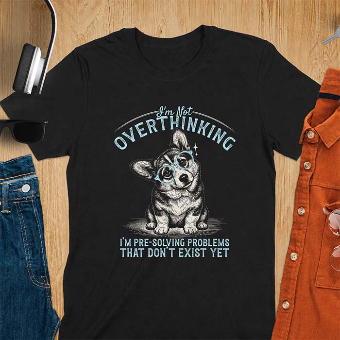 Black t-shirt with a vintage-style illustration of a corgi wearing round glasses, and the text I'm Not Overthinking, I'm Pre-Solving Problems That Do Not Exist Yet.