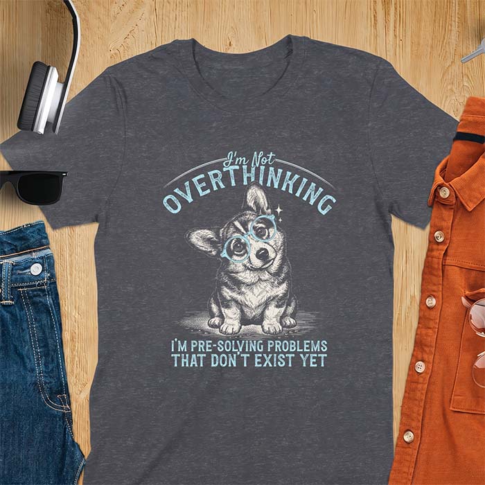 Dark Heather t-shirt with a vintage-style illustration of a corgi wearing round glasses, and the text I'm Not Overthinking, I'm Pre-Solving Problems That Do Not Exist Yet.