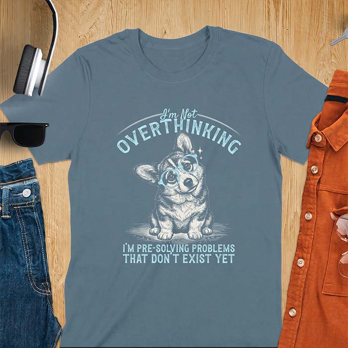 Indigo Blue t-shirt with a vintage-style illustration of a corgi wearing round glasses, and the text I'm Not Overthinking, I'm Pre-Solving Problems That Do Not Exist Yet.