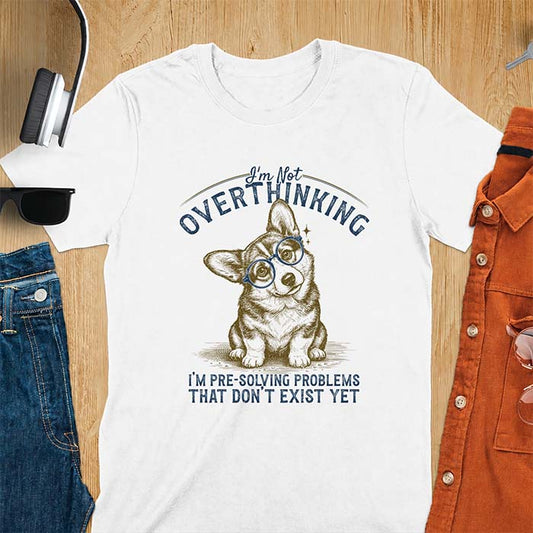 White t-shirt with a vintage-style illustration of a corgi wearing round glasses, and the text I'm Not Overthinking, I'm Pre-Solving Problems That Do Not Exist Yet.