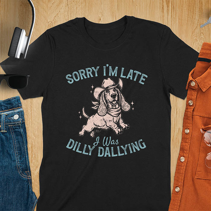 Black t-shirt featuring a galloping basset hound wearing a cowboy hat with long floppy ears flowing, text reads Sorry I'm Late I Was Dilly Dallying