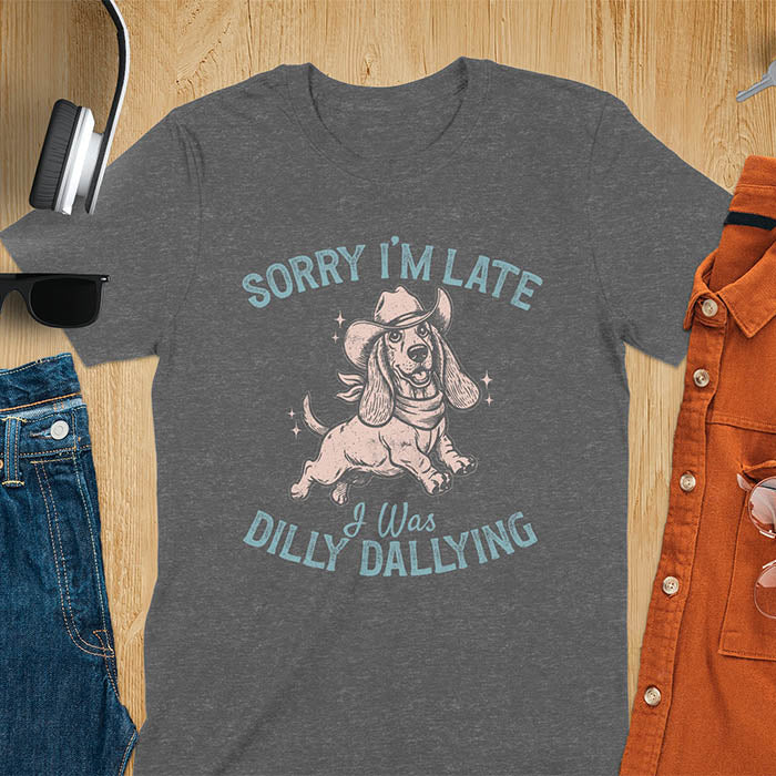 Dark heather t-shirt featuring a galloping basset hound wearing a cowboy hat with long floppy ears flowing, text reads Sorry I'm Late I Was Dilly Dallying