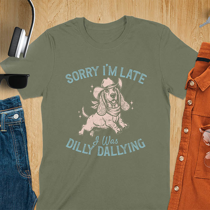 Military Green t-shirt featuring a galloping basset hound wearing a cowboy hat with long floppy ears flowing, text reads Sorry I'm Late I Was Dilly Dallying