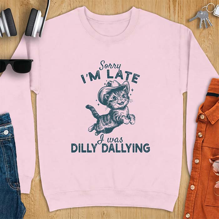 Light Pink sweatshirt with a graphic of a kitten wearing a cowboy hat leaping through the air with sparkle accents and the text Sorry I'm Late I Was Dilly Dallying