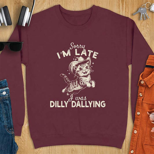 Maroon sweatshirt with a graphic of a kitten wearing a cowboy hat leaping through the air with sparkle accents and the text Sorry I'm Late I Was Dilly Dallying