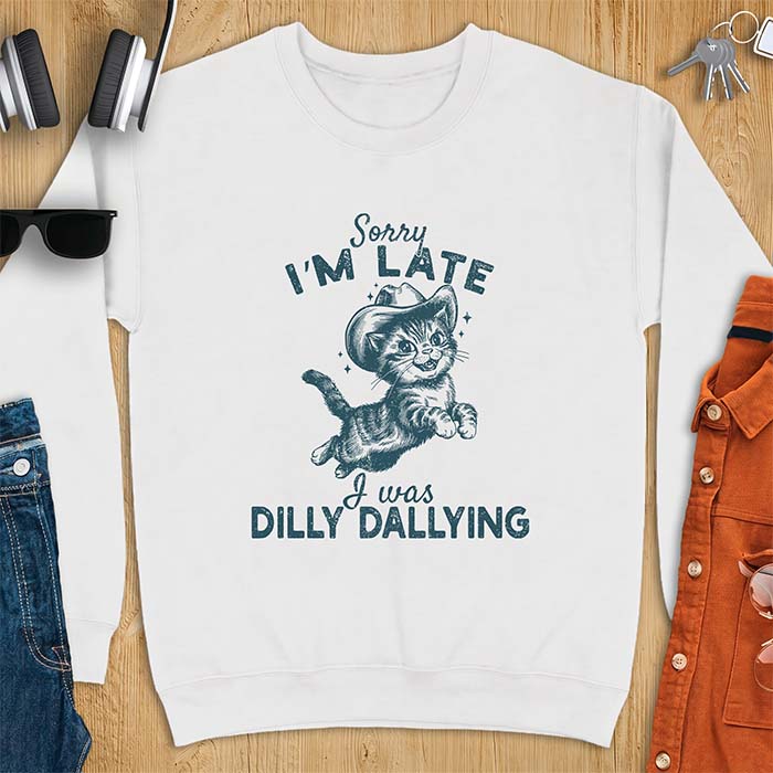 White sweatshirt with a graphic of a kitten wearing a cowboy hat leaping through the air with sparkle accents and the text Sorry I'm Late I Was Dilly Dallying