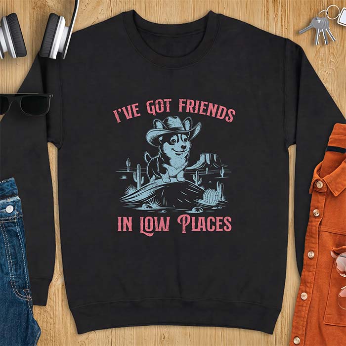 Black sweatshirt with a western graphic of a corgi puppy in a cowboy hat standing on a desert rock surrounded by cacti and a mesa, with the text I've Got Friends In Low Places printed above and below it.