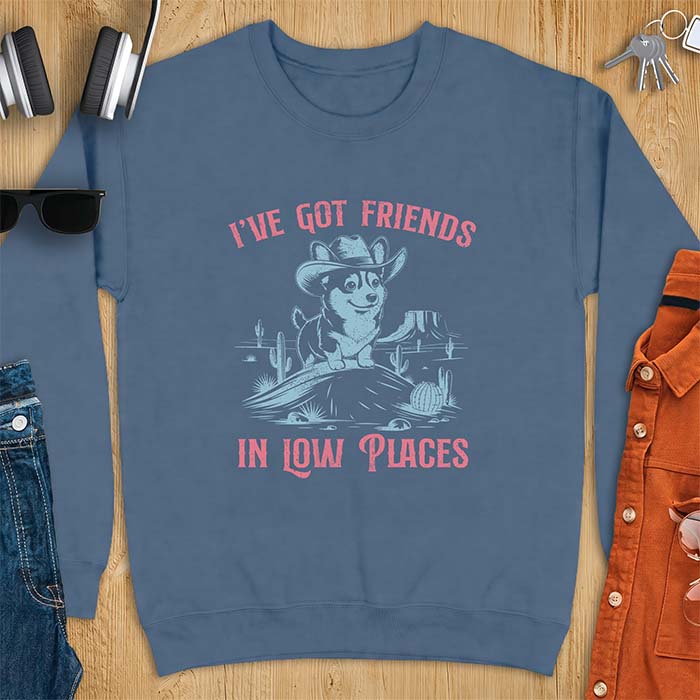 Indigo Blue sweatshirt with a western graphic of a corgi puppy in a cowboy hat standing on a desert rock surrounded by cacti and a mesa, with the text I've Got Friends In Low Places printed above and below it.