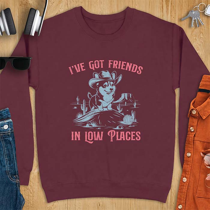 Maroon sweatshirt with a western graphic of a corgi puppy in a cowboy hat standing on a desert rock surrounded by cacti and a mesa, with the text I've Got Friends In Low Places printed above and below it.