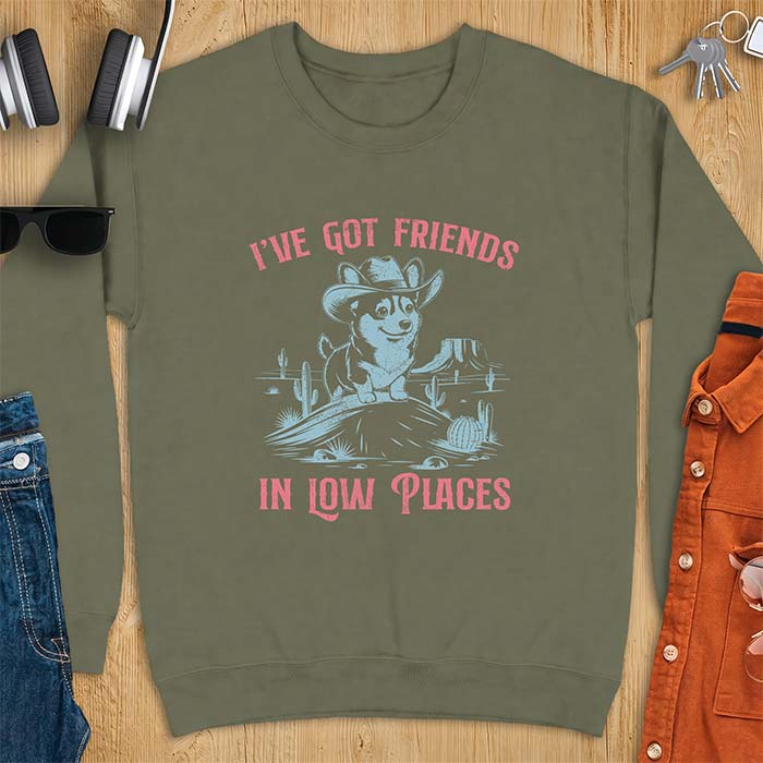 Military Green sweatshirt with a western graphic of a corgi puppy in a cowboy hat standing on a desert rock surrounded by cacti and a mesa, with the text I've Got Friends In Low Places printed above and below it.