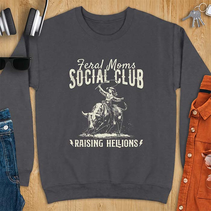 Dark heather sweatshirt with a vintage western graphic of a cowgirl riding a bucking bull and swinging a whip, with the text Feral Moms Social Club above and Raising Hellions below
