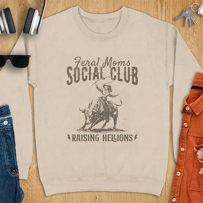 Sand sweatshirt with a vintage western graphic of a cowgirl riding a bucking bull and swinging a whip, with the text Feral Moms Social Club above and Raising Hellions below