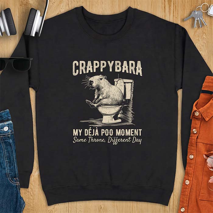 Black sweatshirt with a toilet humor graphic of a capybara sitting on an old-fashioned toilet, printed with the words Crappybara, My Deja Poo Moment, Same Throne, Different Day.