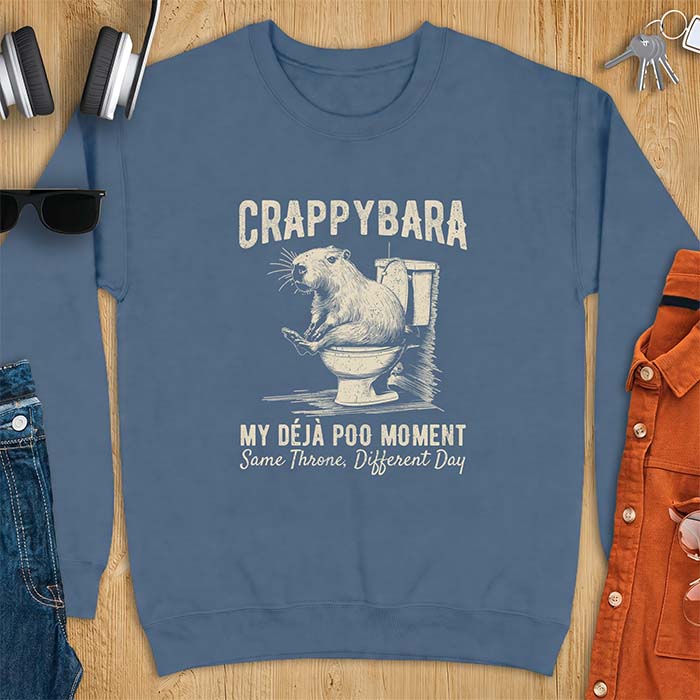 Indigo Blue sweatshirt with a toilet humor graphic of a capybara sitting on an old-fashioned toilet, printed with the words Crappybara, My Deja Poo Moment, Same Throne, Different Day.