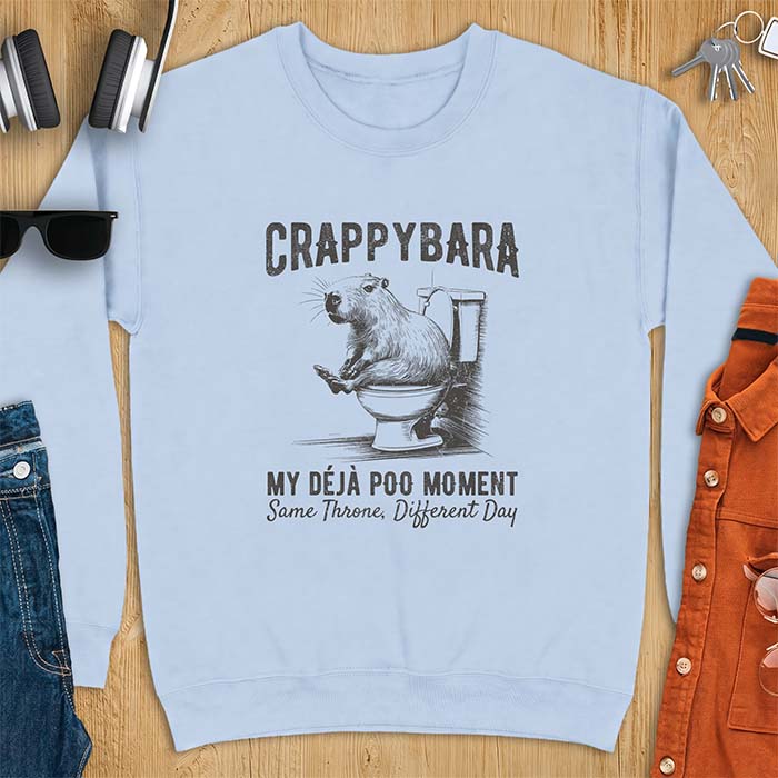 Light Blue sweatshirt with a toilet humor graphic of a capybara sitting on an old-fashioned toilet, printed with the words Crappybara, My Deja Poo Moment, Same Throne, Different Day.