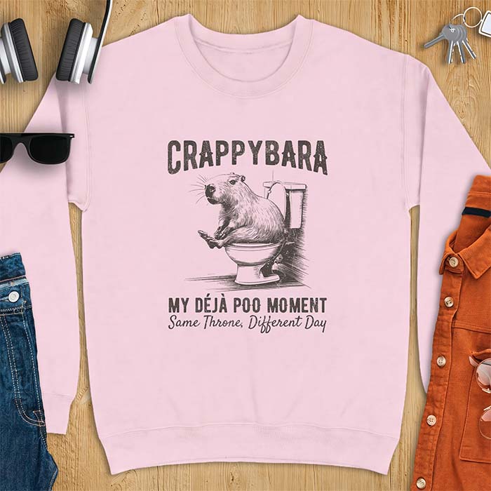 Light Pink sweatshirt with a toilet humor graphic of a capybara sitting on an old-fashioned toilet, printed with the words Crappybara, My Deja Poo Moment, Same Throne, Different Day.