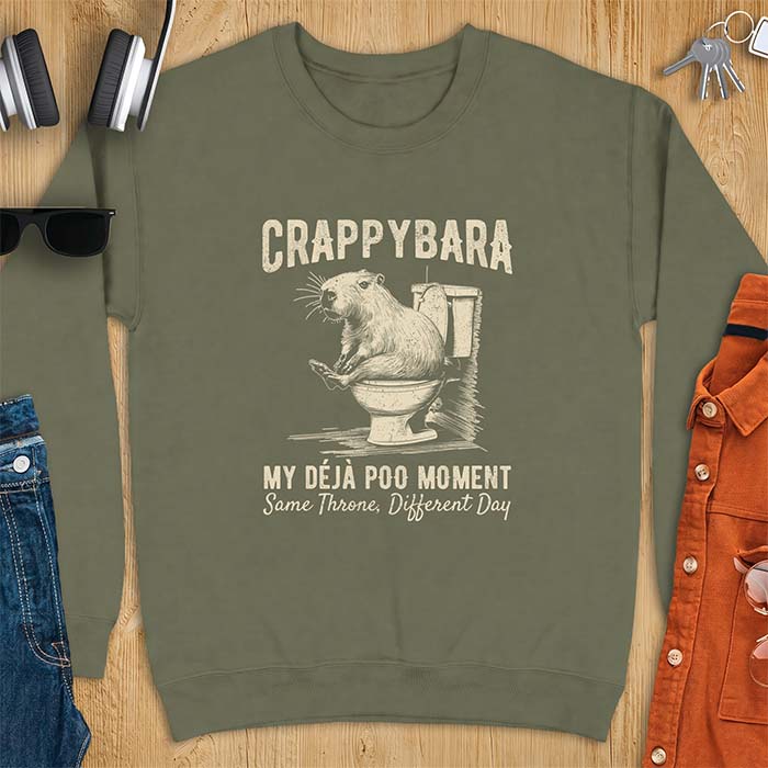 Military Green sweatshirt with a toilet humor graphic of a capybara sitting on an old-fashioned toilet, printed with the words Crappybara, My Deja Poo Moment, Same Throne, Different Day.