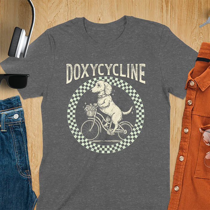 Dark heather Dachshund t-shirt with 'DOXYCYCLINE' text and cute wiener dog riding bicycle in checkered circle design