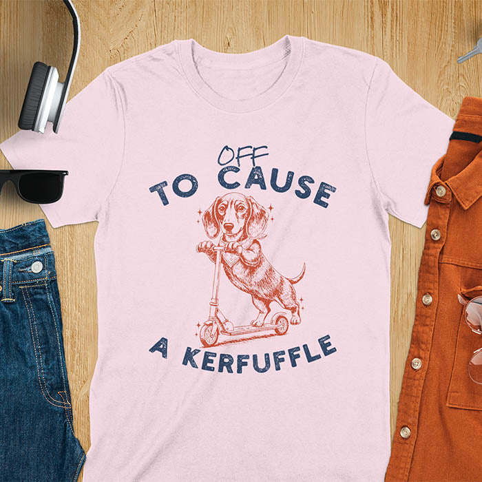 Dachshund on kick scooter illustrated graphic with Off To Cause A Kerfuffle text on light pink t-shirt
