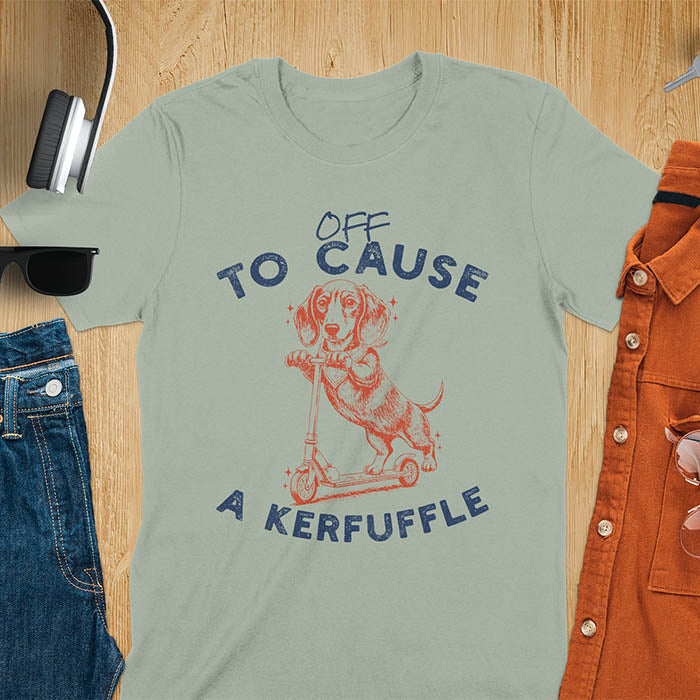 Dachshund on kick scooter illustrated graphic with Off To Cause A Kerfuffle text on sage green t-shirt
