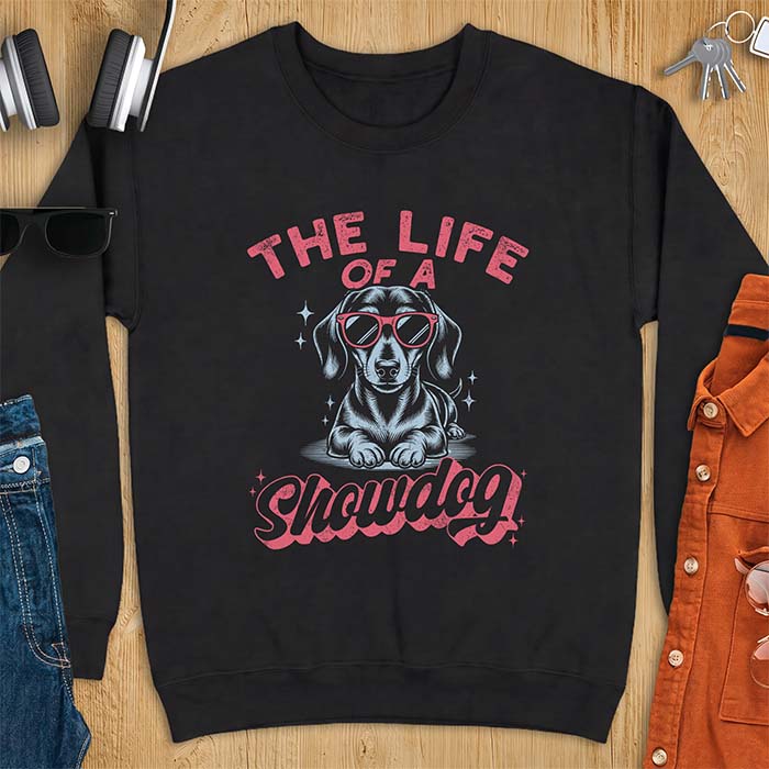 Black sweatshirt with a graphic of a Dachshund wearing red sunglasses lying down surrounded by sparkles, with the text The Life Of A Showdog