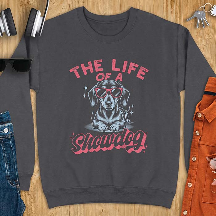 Dark Heather sweatshirt with a graphic of a Dachshund wearing red sunglasses lying down surrounded by sparkles, with the text The Life Of A Showdog