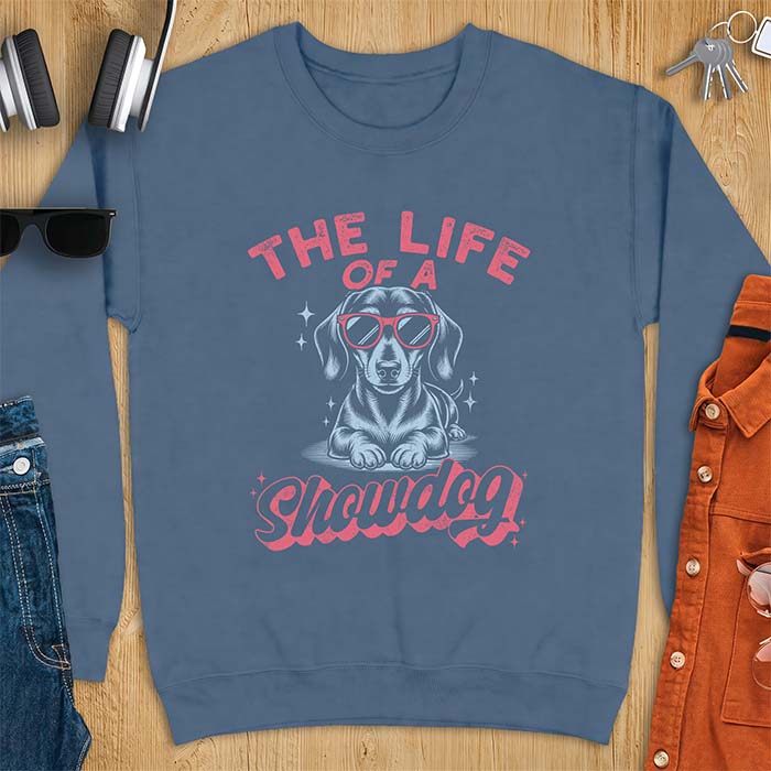 Indigo Blue sweatshirt with a graphic of a Dachshund wearing red sunglasses lying down surrounded by sparkles, with the text The Life Of A Showdog