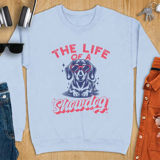 Light Blue sweatshirt with a graphic of a Dachshund wearing red sunglasses lying down surrounded by sparkles, with the text The Life Of A Showdog