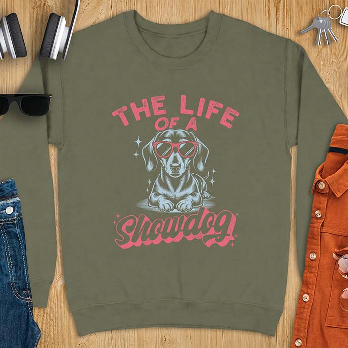 Military Green sweatshirt with a graphic of a Dachshund wearing red sunglasses lying down surrounded by sparkles, with the text The Life Of A Showdog