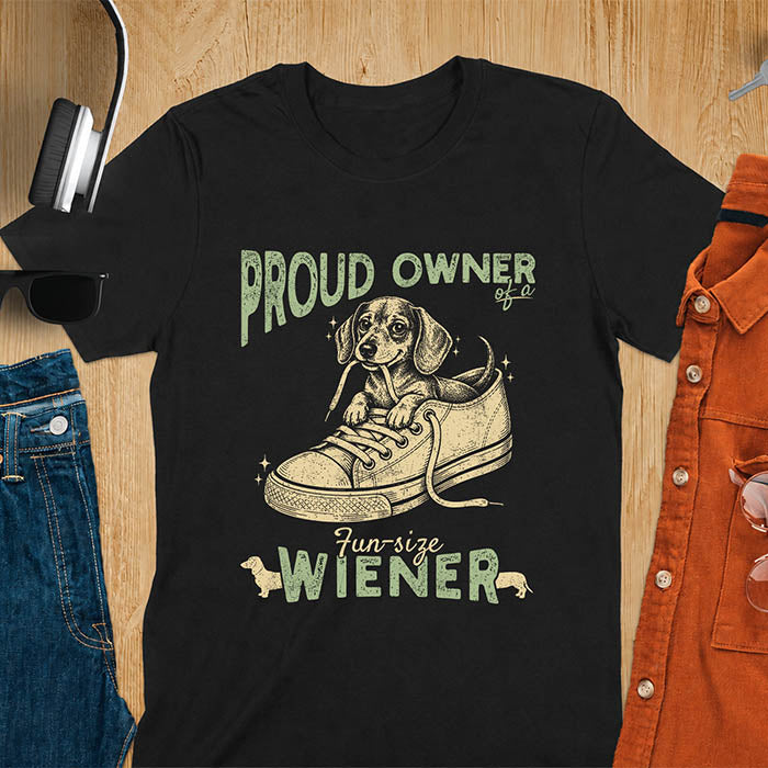 Black unisex t-shirt with a vintage dachshund graphic of a wiener dog pup sitting inside a classic sneaker, with retro bold lettering reading Proud Owner of a Fun-Size Wiener