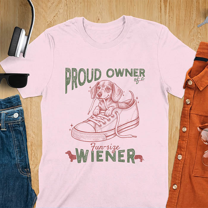 Light Pink unisex t-shirt with a vintage dachshund graphic of a wiener dog pup sitting inside a classic sneaker, with retro bold lettering reading Proud Owner of a Fun-Size Wiener