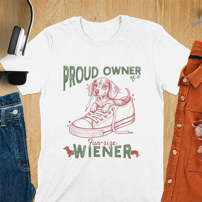 White unisex t-shirt with a vintage dachshund graphic of a wiener dog pup sitting inside a classic sneaker, with retro bold lettering reading Proud Owner of a Fun-Size Wiener