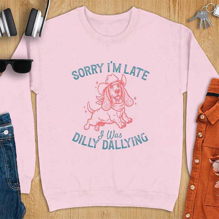 Light Pink sweatshirt with a graphic of a basset hound wearing a cowboy hat and bandana trotting with sparkles around it and the text Sorry I'm Late I Was Dilly Dallying