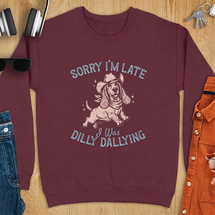 Maroon sweatshirt with a graphic of a basset hound wearing a cowboy hat and bandana trotting with sparkles around it and the text Sorry I'm Late I Was Dilly Dallying