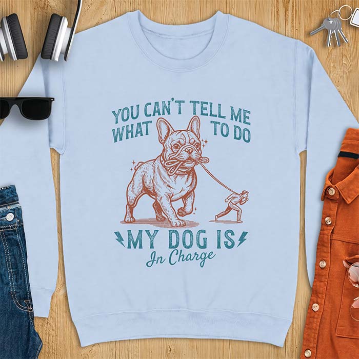 Light Blue sweatshirt with a graphic of a French Bulldog walking a smaller man by the leash and the text “You Can’t Tell Me What To Do. My Dog Is In Charge.”