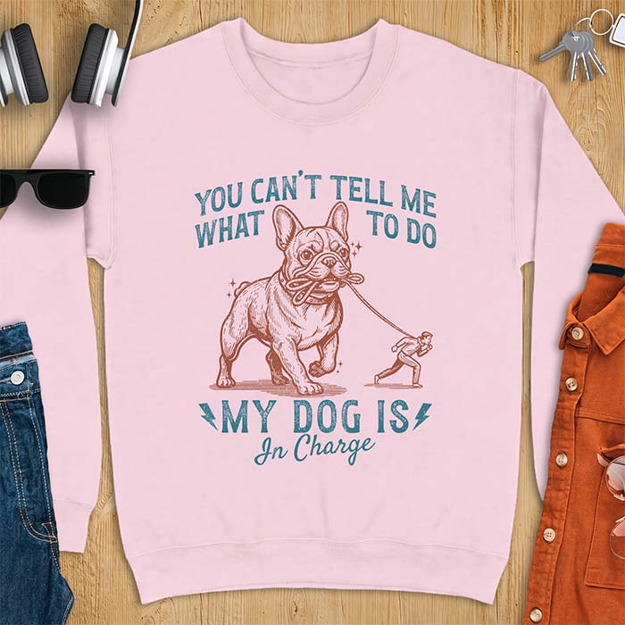 Light Pink sweatshirt with a graphic of a French Bulldog walking a smaller man by the leash and the text “You Can’t Tell Me What To Do. My Dog Is In Charge.”