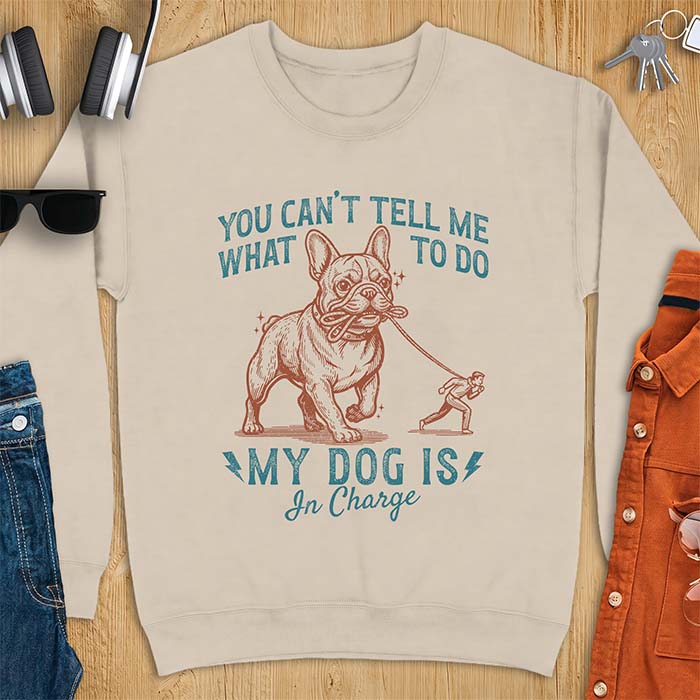 Sand sweatshirt with a graphic of a French Bulldog walking a smaller man by the leash and the text “You Can’t Tell Me What To Do. My Dog Is In Charge.”