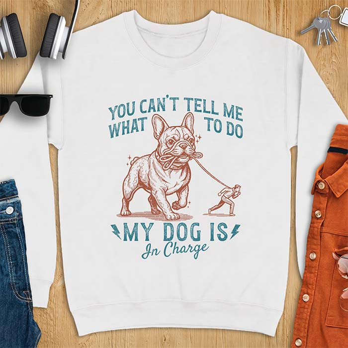White sweatshirt with a graphic of a French Bulldog walking a smaller man by the leash and the text “You Can’t Tell Me What To Do. My Dog Is In Charge.”