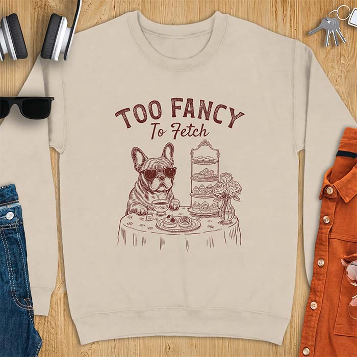 Sand sweatshirt with a graphic of a French Bulldog wearing sunglasses at a table set for high tea beside a teacup and pastry stand, with the text Too Fancy To Fetch