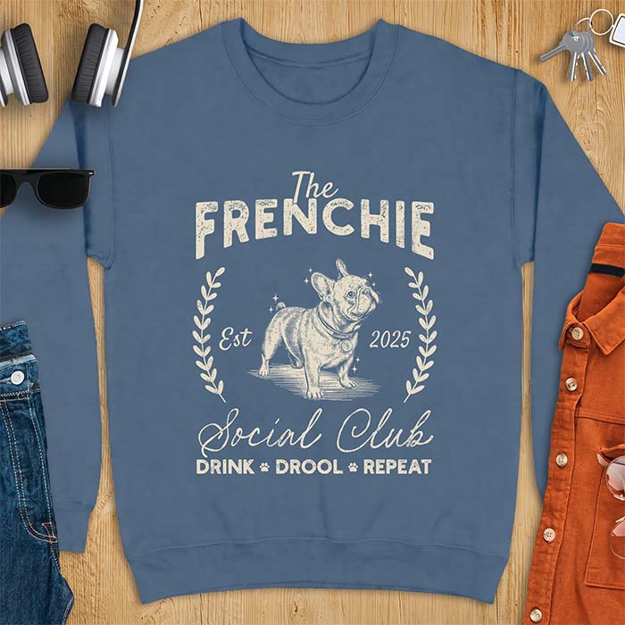 Indigo Blue sweatshirt with a vintage badge graphic of a French Bulldog wearing a collar and tag framed by a laurel wreath, and the text The Frenchie, Est 2025, Social Club, Drink Drool Repeat