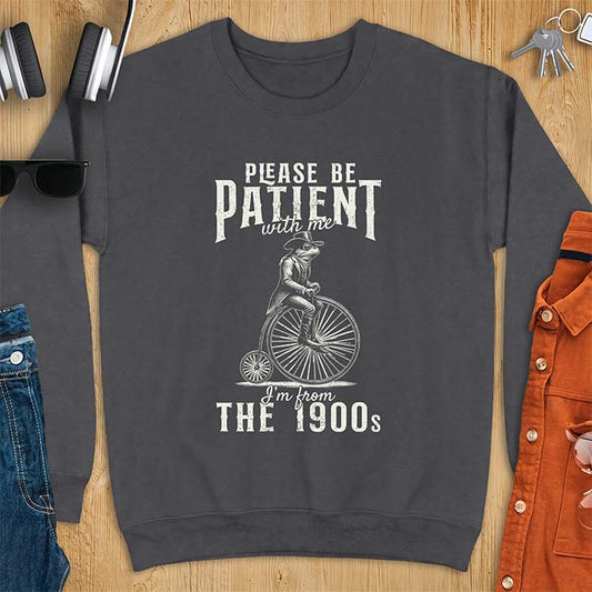 Dark Heather sweatshirt with a graphic of a frog dressed in a Victorian coat, vest, top hat and monocle riding a penny farthing bicycle and the text Please Be Patient With Me I'm From The 1900s