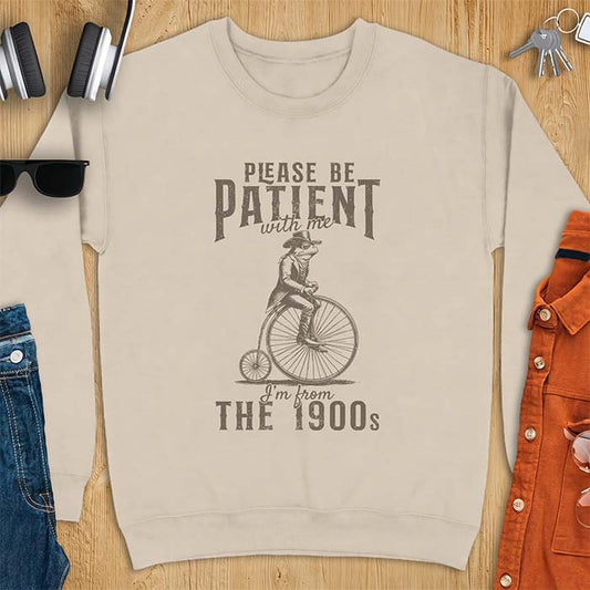 Sand sweatshirt with a graphic of a frog dressed in a Victorian coat, vest, top hat and monocle riding a penny farthing bicycle and the text Please Be Patient With Me I'm From The 1900s